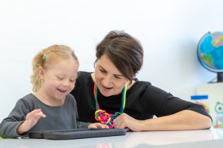 Female toddler in occupational therapy session doing playful exercises on a digital tablet with her occupational therapist.