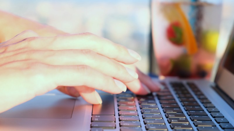Woman's hands typing on a keyboard outdoors