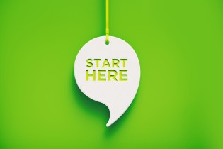 White cardboard cutout of a comma with the words "Start here" carved into it as it rests against a bright green backdrop.