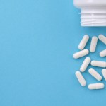 White medication bottle spills 12 white capsules on a light blue background.