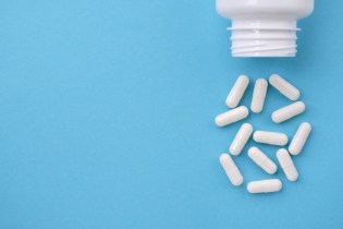 White medication bottle spills 12 white capsules on a light blue background.
