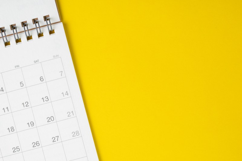 White spiral bound calendar planner against bright yellow background.