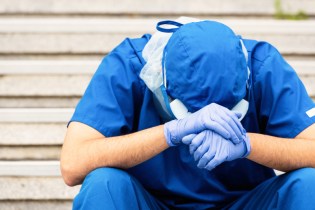 healthcare worker in blue scrubs with head down