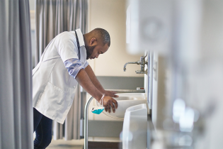 Stressed male African-American healthcare worker leaning over sink with eyes closed.