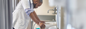 Stressed male African-American healthcare worker leaning over sink with eyes closed.