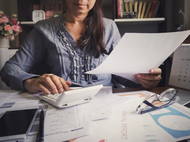 woman typing on calculator looking at papers on desk while researching other types of insurance needed for tax preparers