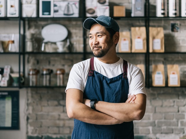 man in an apron and hat with arms folded in front of cafe wall asking himself, "How much general liability insurance coverage do I need"