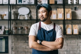 man in an apron and hat with arms folded in front of cafe wall asking himself, "How much general liability insurance coverage do I need"