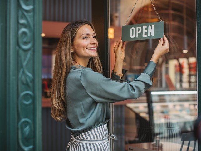 Woman hanging up an open sign outside her business while she thinks about BOP vs GL